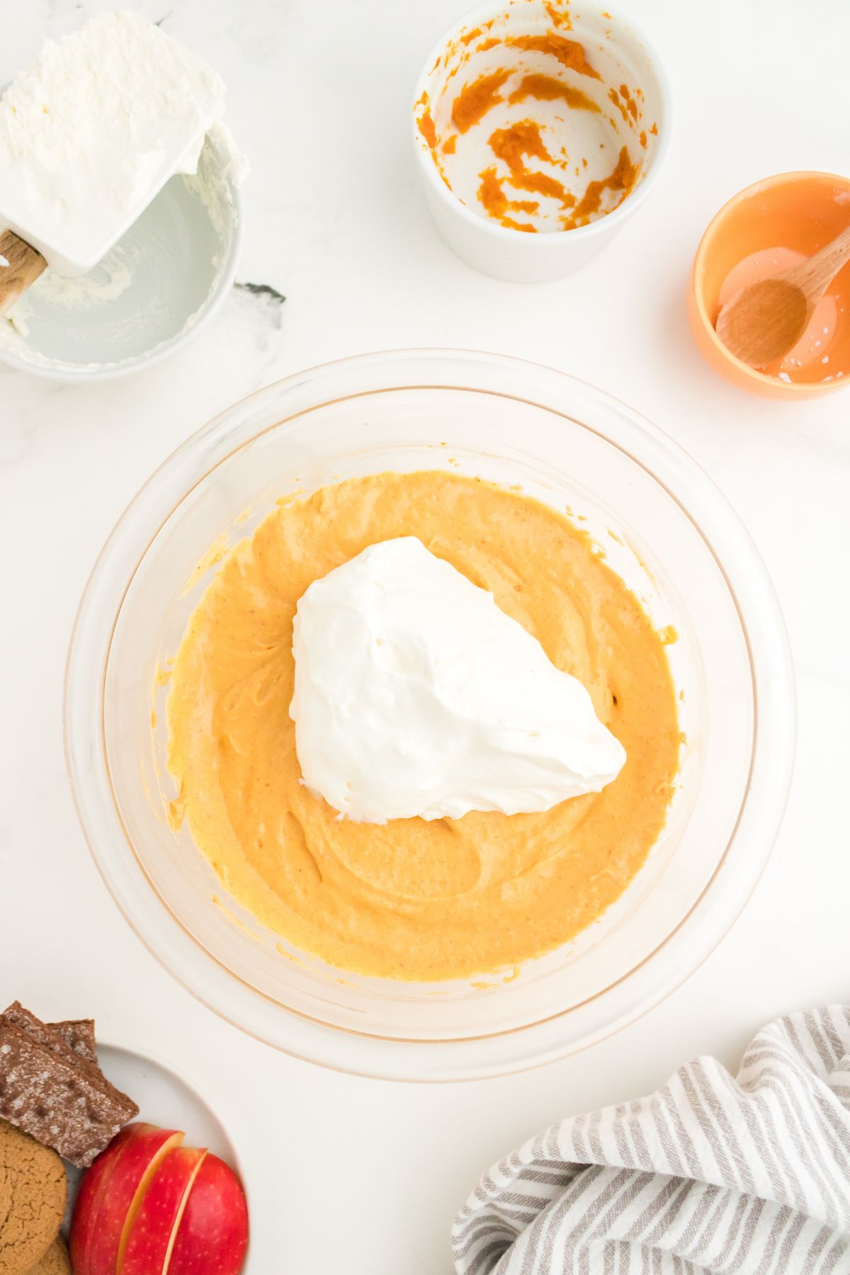 Whipped topping on top of a mixing bowl with pumpkin, cream cheese, powdered sugar, and cinnamon mixed together.