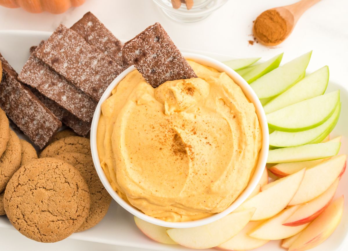 Looking down on a spread of graham crackers, ginger snaps, and apple slices with a bowl of Pumpkin Dip.