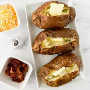 baked potatoes made in the air fryer served with salt, butter, cheese, and bacon