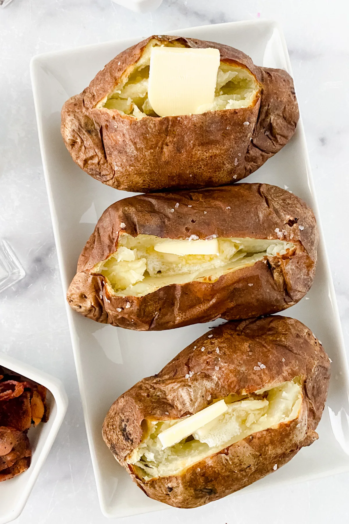 baked potatoes made in the air fryer served with salt, butter, cheese, and bacon