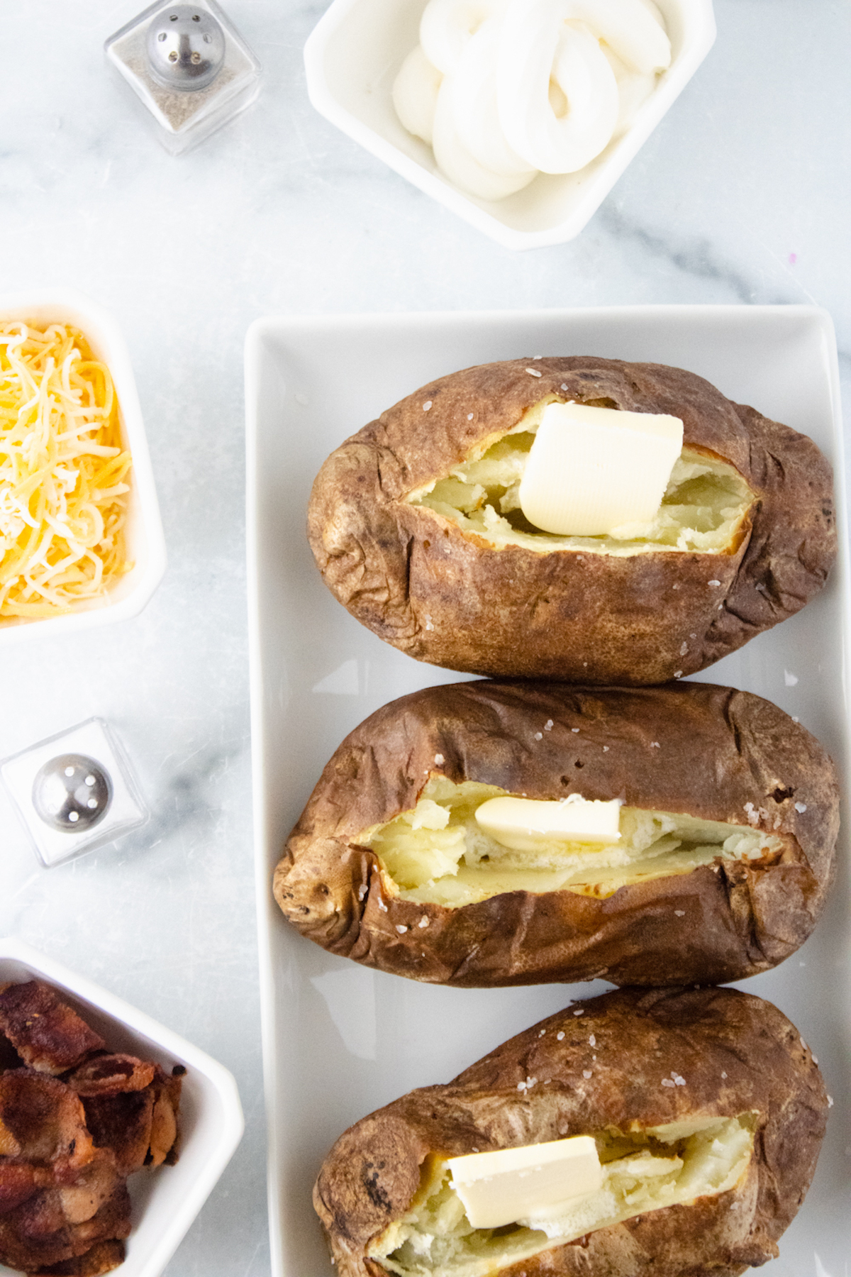 baked potatoes made in the air fryer served with salt, butter, cheese, and bacon
