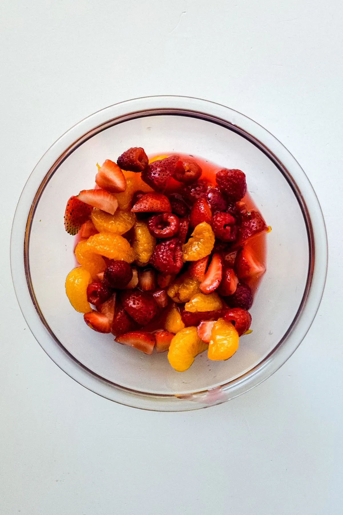 A bowl of mandarin orange slices, raspberries, strawberry slices, and dressing.