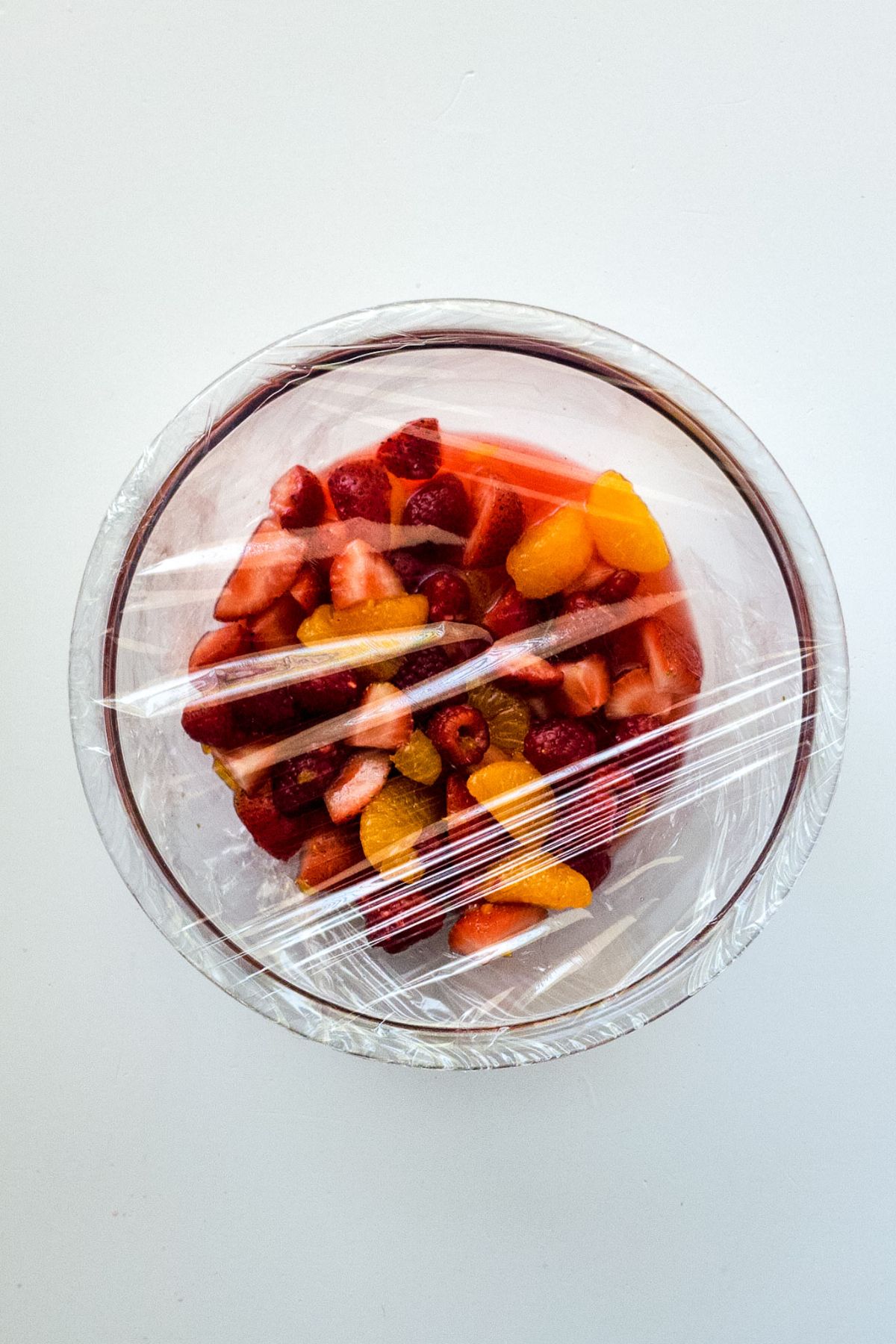 A bowl of fruit salad covered with plastic wrap.