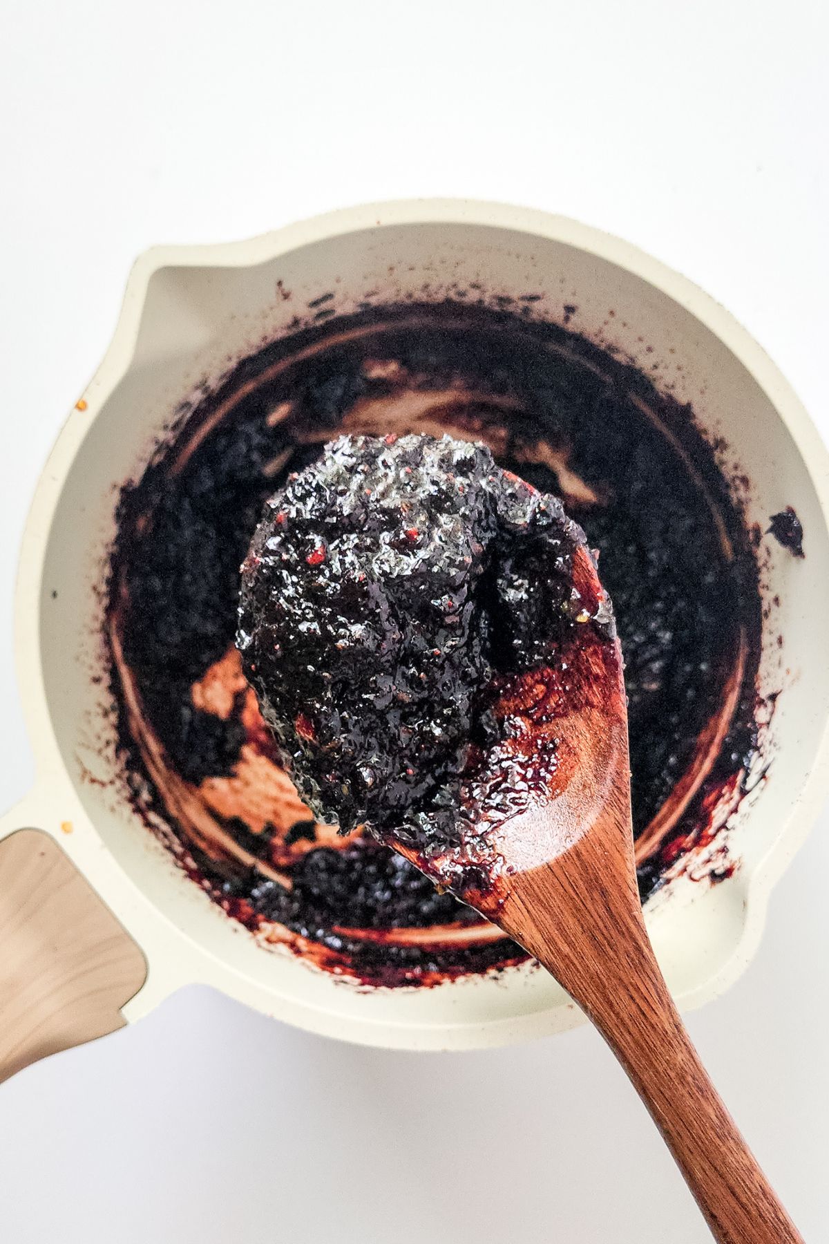 A wooden spoon holding some mixed berry jam over the pan with more.