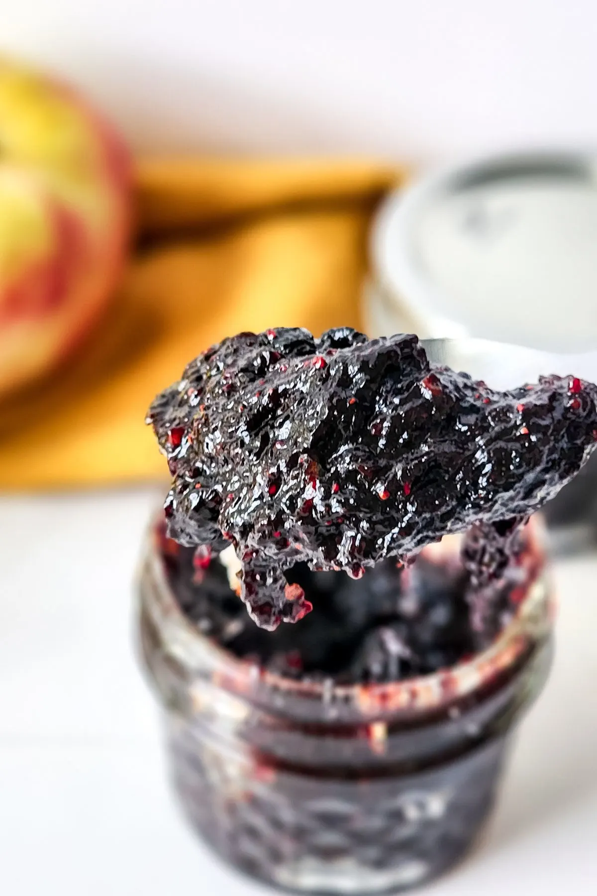 A spoon holding some mixed berry jam over the jar.