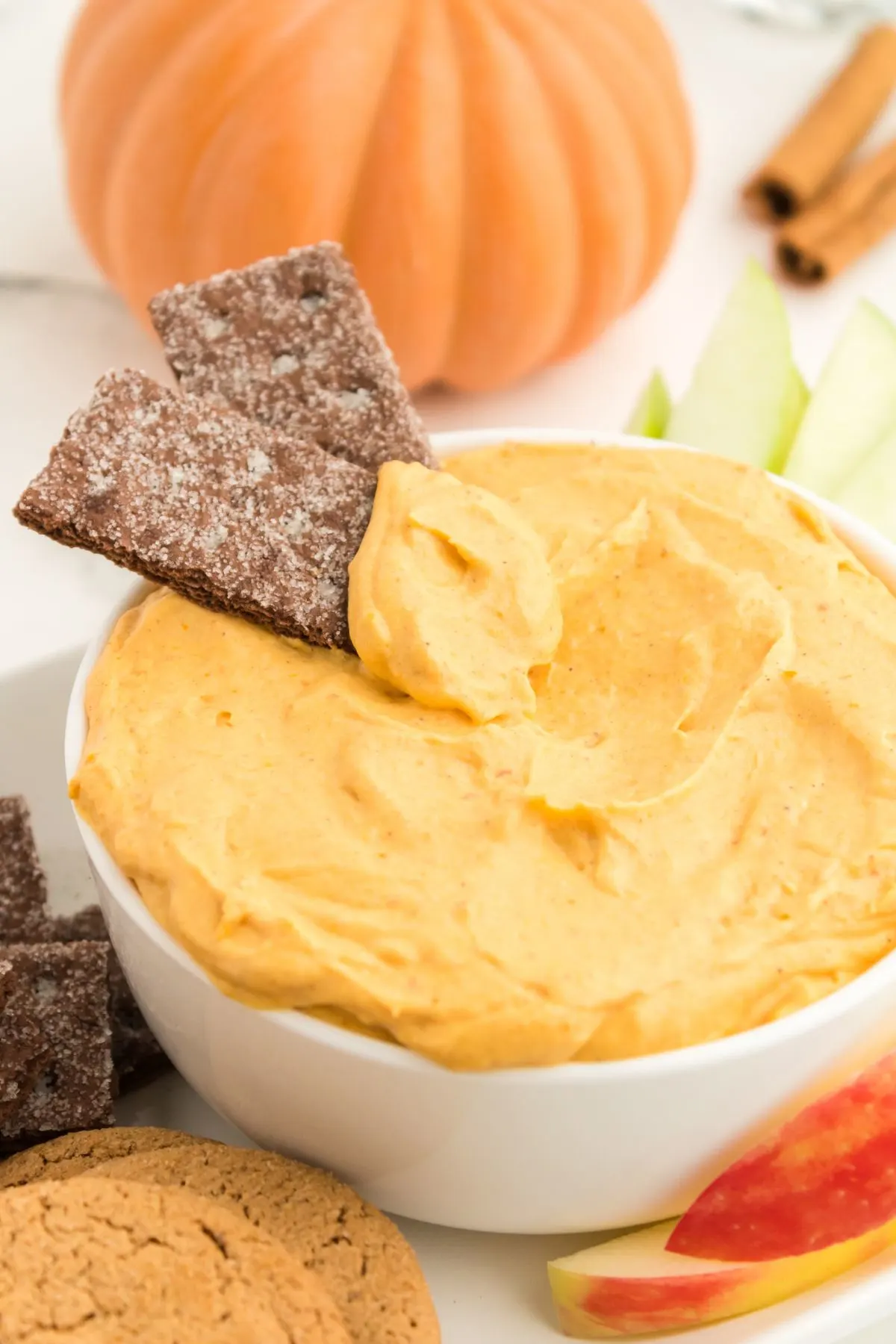 A white bowl of Pumpkin Dip with two chocolate graham crackers dipped in it.
