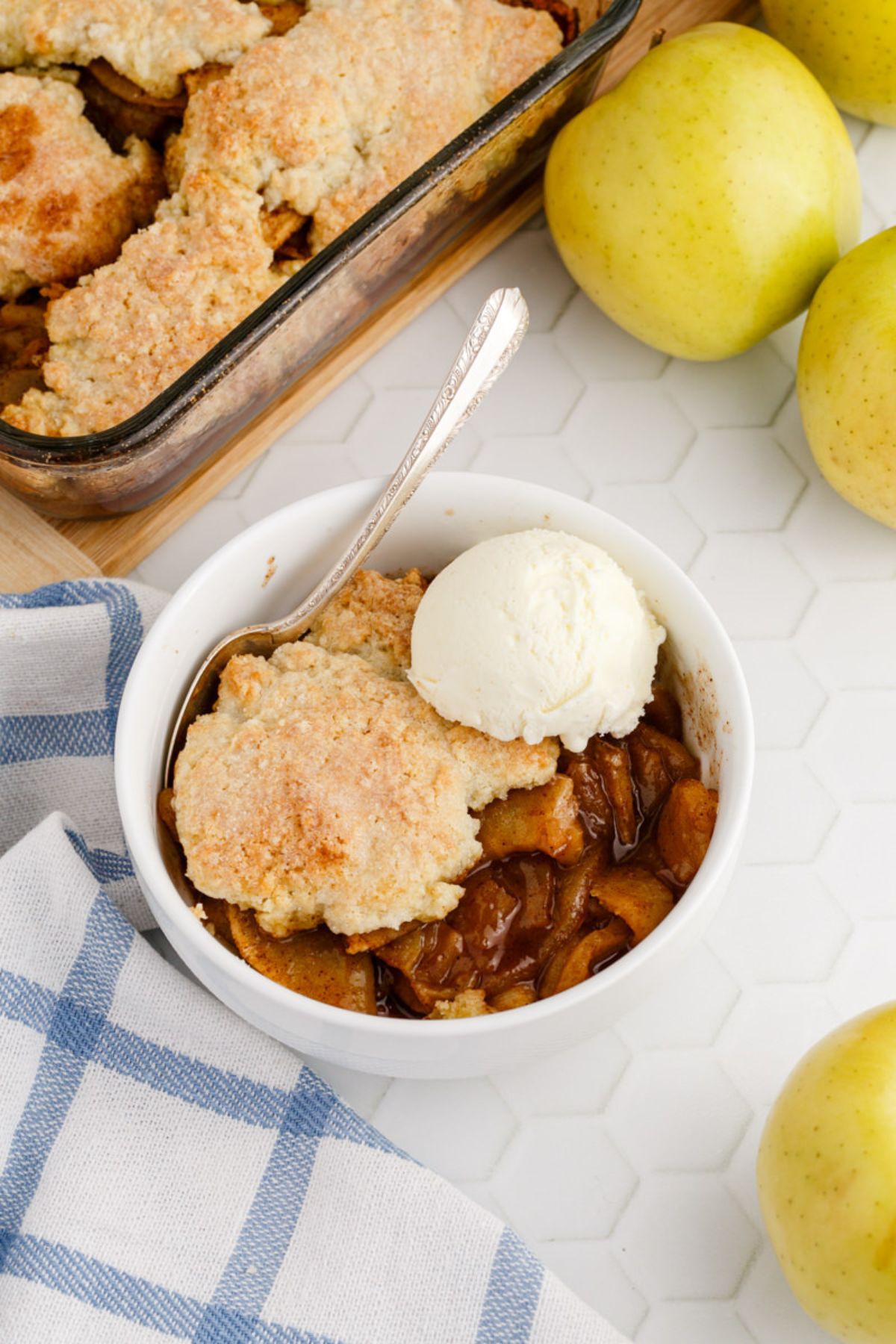 A serving of Apple Cobbler in a white bowl with a scoop of vanilla ice cream.
