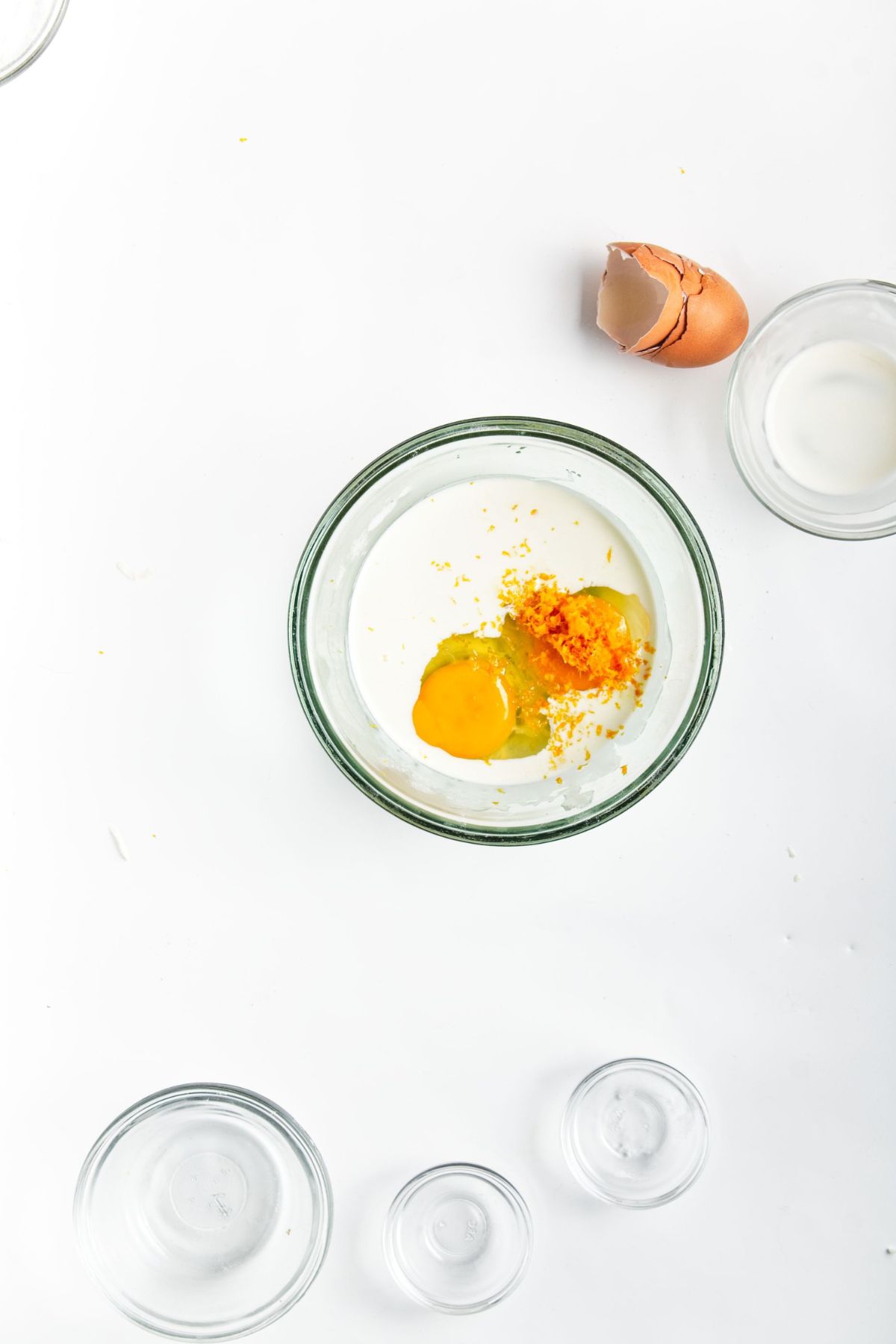 A mixing bowl with eggs, cream and orange zest.